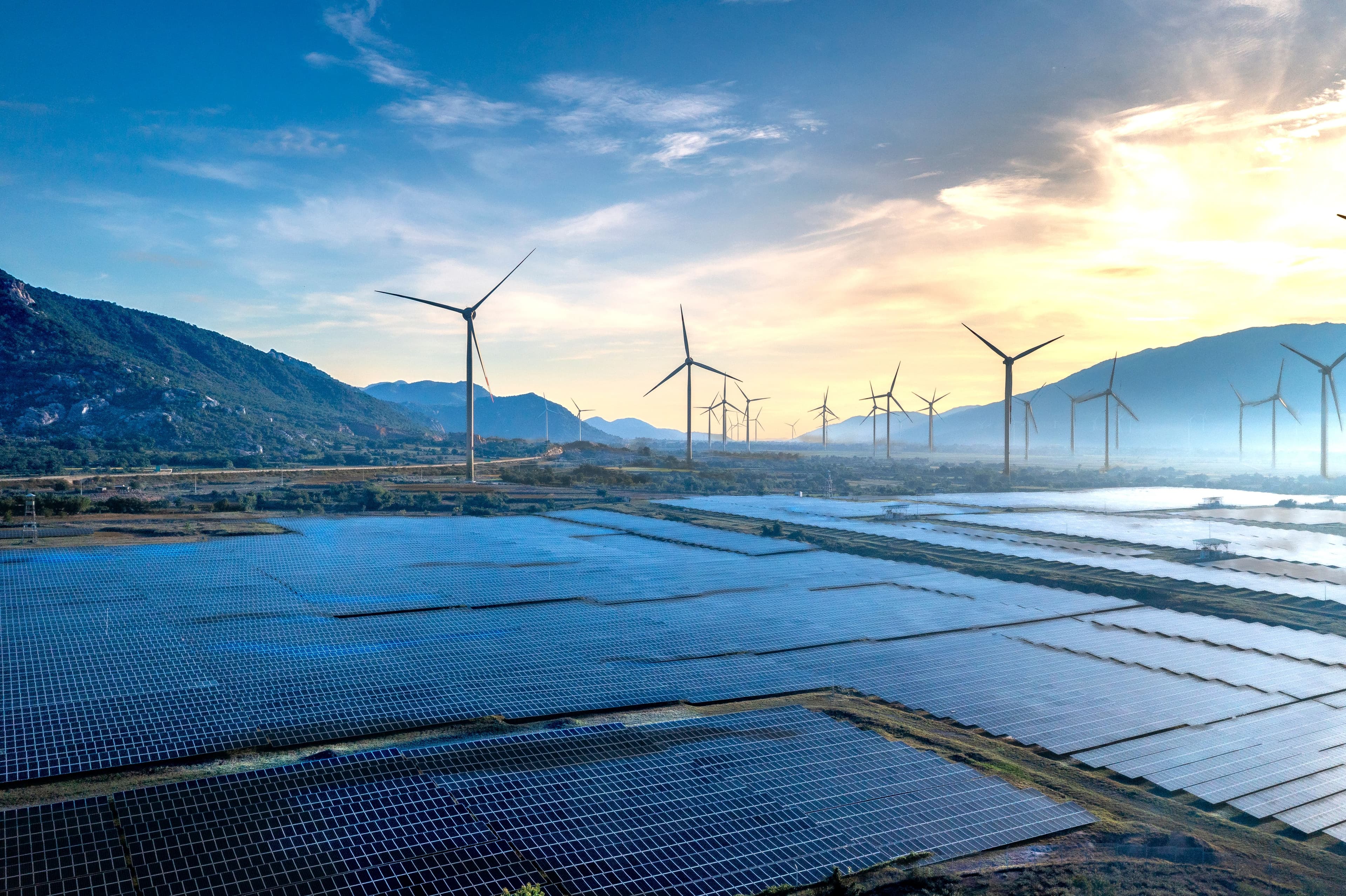 Solar panels and wind turbines producing renewable electricity at sunrise